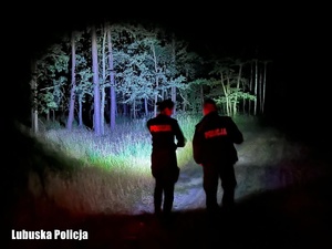 policjanci w lesie po zmroku oświetlają teren latarkami