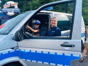 dziewczynka z namalowaną buzia kotka siedzi za kierownicą policyjnego radiowozu a przy niej policjantka