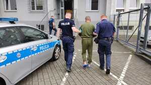 osoba zatrzymana z założonymi kajdankami zespolonymi na ręce i nogi  prowadzona przez funkcjonariuszy do budynku Komendy Powiatowej Policji w Chr