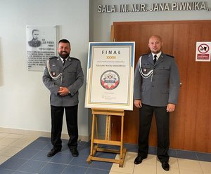 Policjanci w pomieszczeniu stoją w mundurach galowych przy tablicy finał ogólnopolski trzydziestego trzeciego konkursu policjant ruchu drogowego