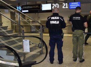 policjant i strażnik graniczny stojący tyłem do zdjęcia, przed nimi strefa bagażowa