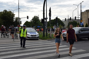 osoby przechodzą przez przejście dla pieszych przed policjatem
