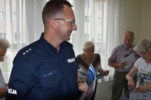 Umundurowany policjant rozdający ulotki informacyjne osobom biorącym udział w profilaktyce