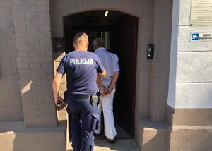 Policjant wprowadzający do aresztu zatrzymanego z kajdankami założonymi na ręce trzymane z tyłu