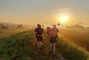 grupa osób biegnie polną ścieżką w tle wschód Słońca