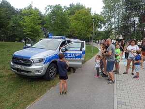 Kolejka dzieci i młodzieży ustawiająca się przy policyjnym radiowozie.