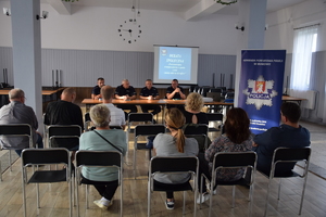 uczestnicy debaty siedzący tyłem do zdjęcia, przed nimi przedstawiciele Policji, za nimi wyświetlona prezentacja, obok po prawej baner KPP w Krakowie