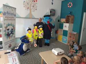 przedszkolaki w elementach umundurowania policyjnego na pamiątkowej fotografii z policjantką i maskotkmi policyjnymi