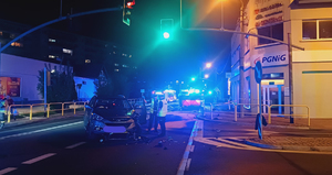 w porze nocnej na skrzyżowaniu z sygnalizacją świetlna stoi rozbity samochód obok samochody stoją umundurowani funkcjonariusze w tle widać rozłoz