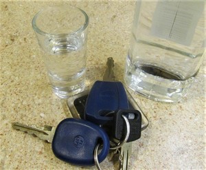 kluczyki do  samochodu, obok kieliszek i butelka z alkoholem