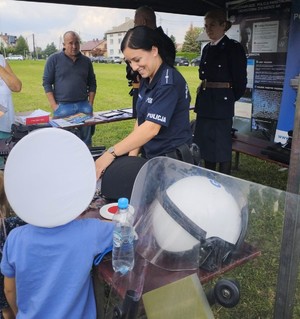 Rajsko piknik historyczno - wojskowy policjantka na stoisku prezentuje sprzęt policyjny dziecko w czarpce policjantaprzed stoiskiem
