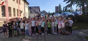 Dwie policjntki z grupą dzieci przed budynkiem szkoły.