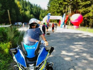 policjant ruchu drogowego na służbowym motocyklu, w tle biegacze