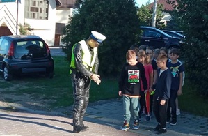 Bezpieczna droga do szkoły dzieci z policjantami z oświęcimskiej komendy policjant i dzieci stoją na chodniku przed szkołą