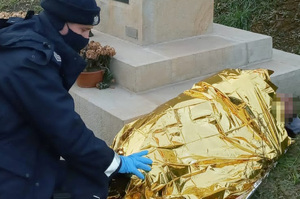 Policjant przykrywa kocem termicznym leżącego mężczyznę