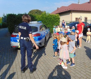policjantka stojąca z grupą przedszkolaków przy radiowozie