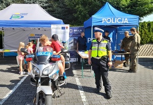 Przeciszów Policyjna Odyseja VI  (7) policjant obok motocykla na motocyklu chłopiec w tle stoisko policyjne