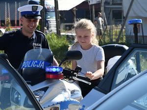 Umundurowany policjant oraz dziecko siedzące na policyjnym motocyklu