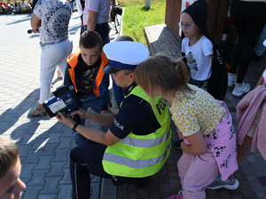 Umunudorwana policjanta mająca na sobie kamizelkę odbalskową oraz czpakę służbową pokazująca dzieciom policyjny sprzęt.