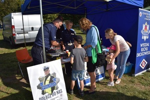 dwie kobiety i dwoje dzieci przy policyjnym stoisku profilaktycznym rozmawiają z policjantem i policjantką