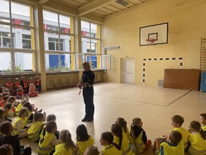 sala gimnastyczna policjantka tłumaczy dzieciom zasady bezpieczeństwa w ruchu drogowym