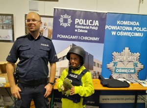policjant z dzieckiem ubranym w kamizelkę i hełm kuloodporny