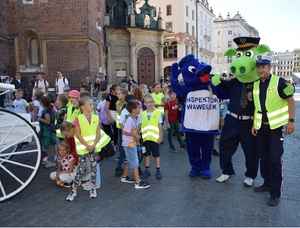 dzieci  idące w marszu, policjant z maskotką Policji i Straży Miejskiej