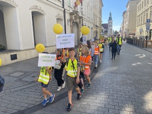dzieci idące w marszu z transparentem z napisem noś odblaski bądź widoczny
