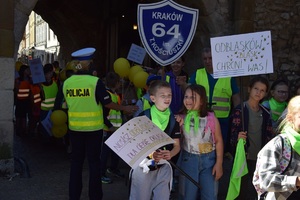 policjantka czuwa nad bezpieczeństwem uczestników marszu dziewczynka trzyma transparent z napisem odblasków  blask chroni was