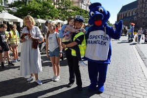 policjantka z dzieckiem na rękach obok maskotka policyjna inspektor Wawelek