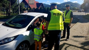 policjanci z dziećmi rozmawiają z kierującą która siedzi w białym samochodzie
