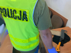 policjant przy stoliku na którym leży zabezpieczona kominiarka i niebezpieczne narzędzie