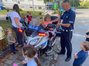 dziewczynka na policyjnym motocyklu, obok stoi policjant, wokół inne przedszkolaki
