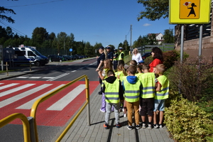 dwoje policjantów, nauczycielki i dzieci w kamizelkach odblaskowych stoją przed przejściem dla pieszych
