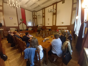 prelekcja w sali narad, uczestnicy siedzący przy stołach wraz z policjantką, na środku prowadzący prelekcje psycholog, za nim wyświetlona prezentacja