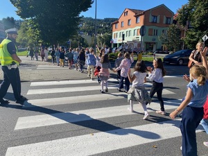 policjant i nauczycielka stojące przy przejściu dla pieszych asekurujący dzieci przechodzące przez drogę