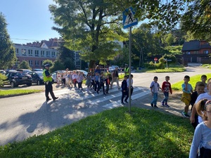 policjant stojący przed przejściem dla pieszych i dzieci przechodzące przez drogę