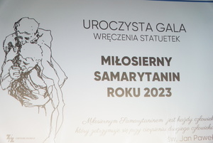 baner wyświetlany w kinie na scenie z napisem samotny samarytanin 2023 roku wraz z hasłem Jana Pawla 2