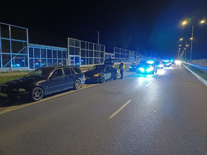 dwa samochody stojące na poboczu drogi w trakcie nocnej policyjnej kontroli. Z tyłu widać radiowozy oraz inne pojazdy