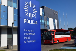 baner Komendy Powiatowej Policji w Krakowie, w tle zaparkowany krwiobus przed komendą