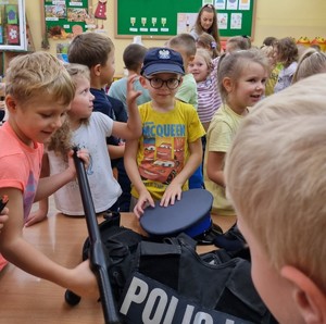spotkanie przedszkolaków z kierownikiem dzielnicowych  (2) dzieci zakładają elementy munduru policjanta oglądają pałkę tonfa