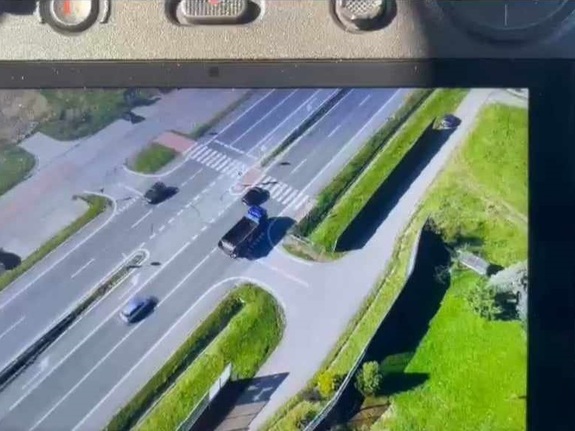 zdjęcie drogi dwujezdniowej na którym widać z góry jak kierujący czarnym samochodem wyprzedza na przejściu dla pieszych ciężarówkę