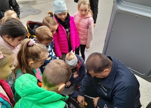 Zwiedzanie komendy Pierwszaki z Brzezinki zastępca naczelnika wydziału prezencji wraz z dziećmi przy radiowozie