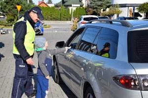 dziecko wraz z policjantem wręcza kierowcy ulotkę