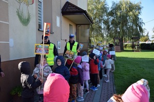 Policjanci wraz z dziećmi pod przedszkolem. Dzieci trzymają transparenty