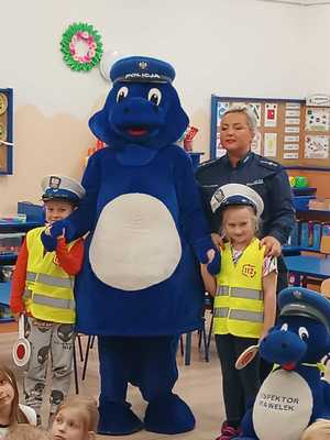 policjantka wraz z dziećmi  w elementach umundurowania policjanta ruchu drogowego oraz maskotki policyjne