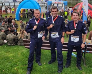 policjanci Ciągło, Wójcik, Ryś po biegu z medalami  w tle inni uczestnicy