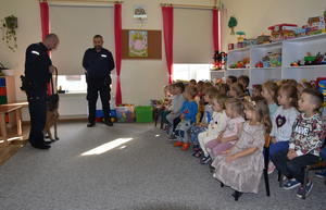 Policjanci, policyjny pies służbowy oraz siedzące na krzesłach dzieci podczas prelekcji