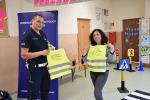 policjant z nauczycielką trzymają kamizelki odblaskowe z napisem bezpieczny powiat krakowski