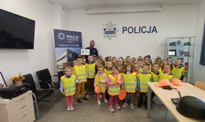 KPP Oświęcim. Przedszkolaki zwiedzanie KP Zator  (3) policjant na wspólnym zdjęciu z przedszkolakami w komisariacie